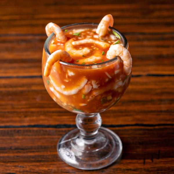 Shrimp cocktail in a large glass, garnished with whole shrimp on a wooden table.