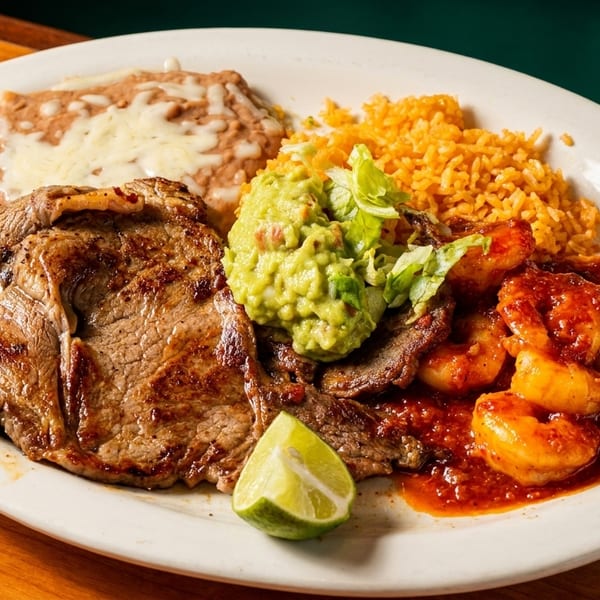 Grilled steak, spicy shrimp, rice, refried beans, guacamole, and a lime wedge on a white plate.