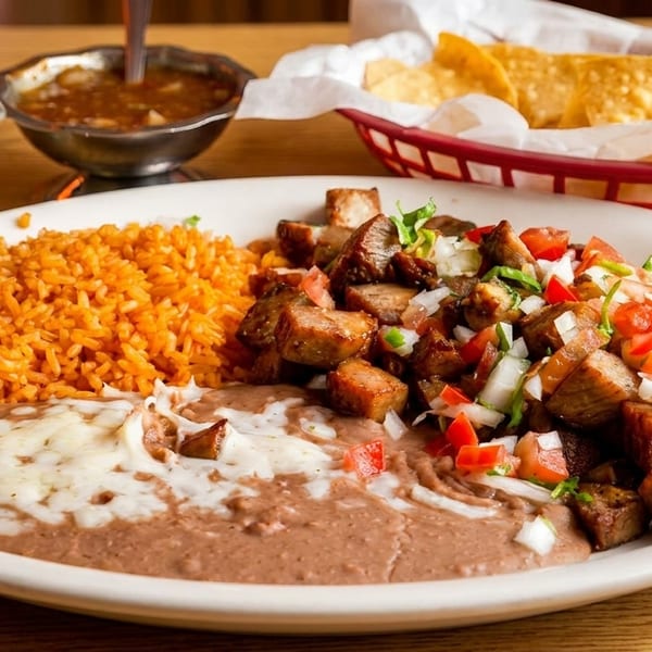 A Mexican dish with rice, refried beans, carnitas, pico de gallo, and a side of chips and salsa.