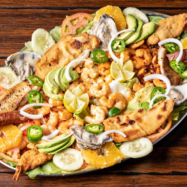 A large platter of seafood with shrimp, oysters, fried fish, avocado, and citrus on a wooden table.