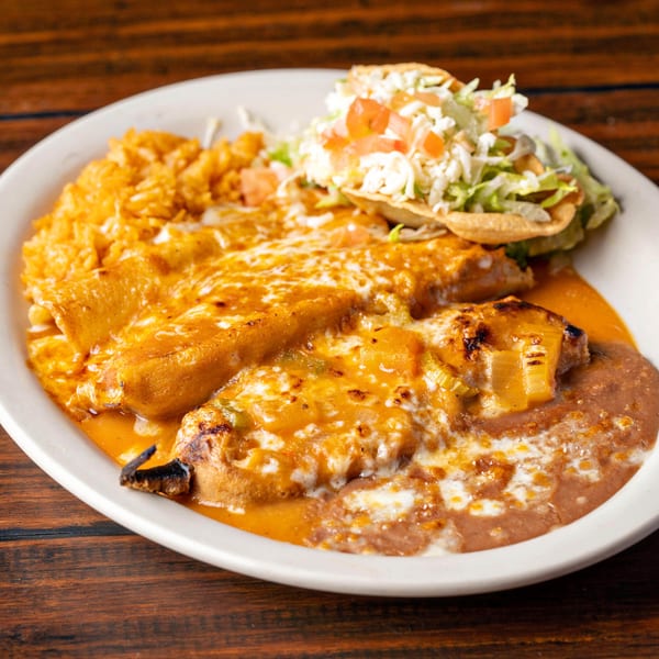 A white plate holds a Mexican combo meal with enchiladas, rice, refried beans, and a tostada.