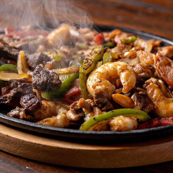 Steaming hot fajitas with shrimp, steak, onions, and bell peppers in a cast iron skillet.
