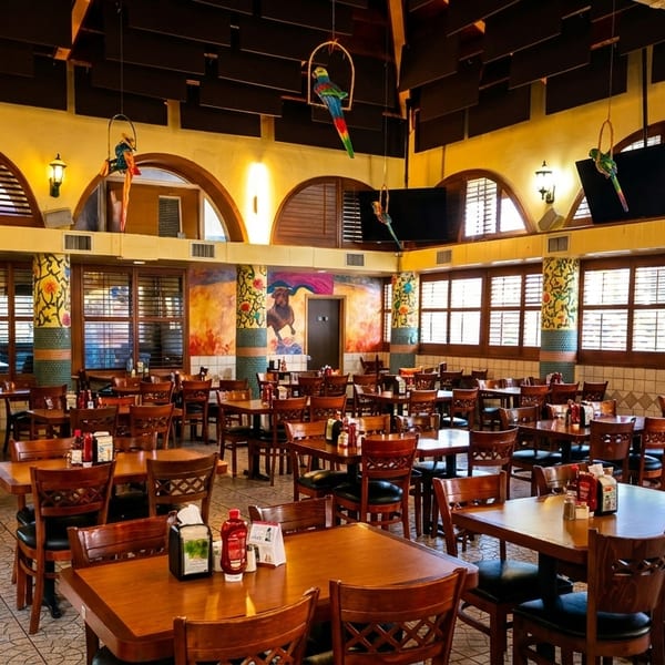 Spacious, colorful restaurant dining room with many empty tables, chairs, and decorative parrots hanging from the ceiling.