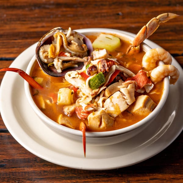Hearty seafood soup with shrimp, crab, clams, and vegetables in a white bowl on a wooden table.