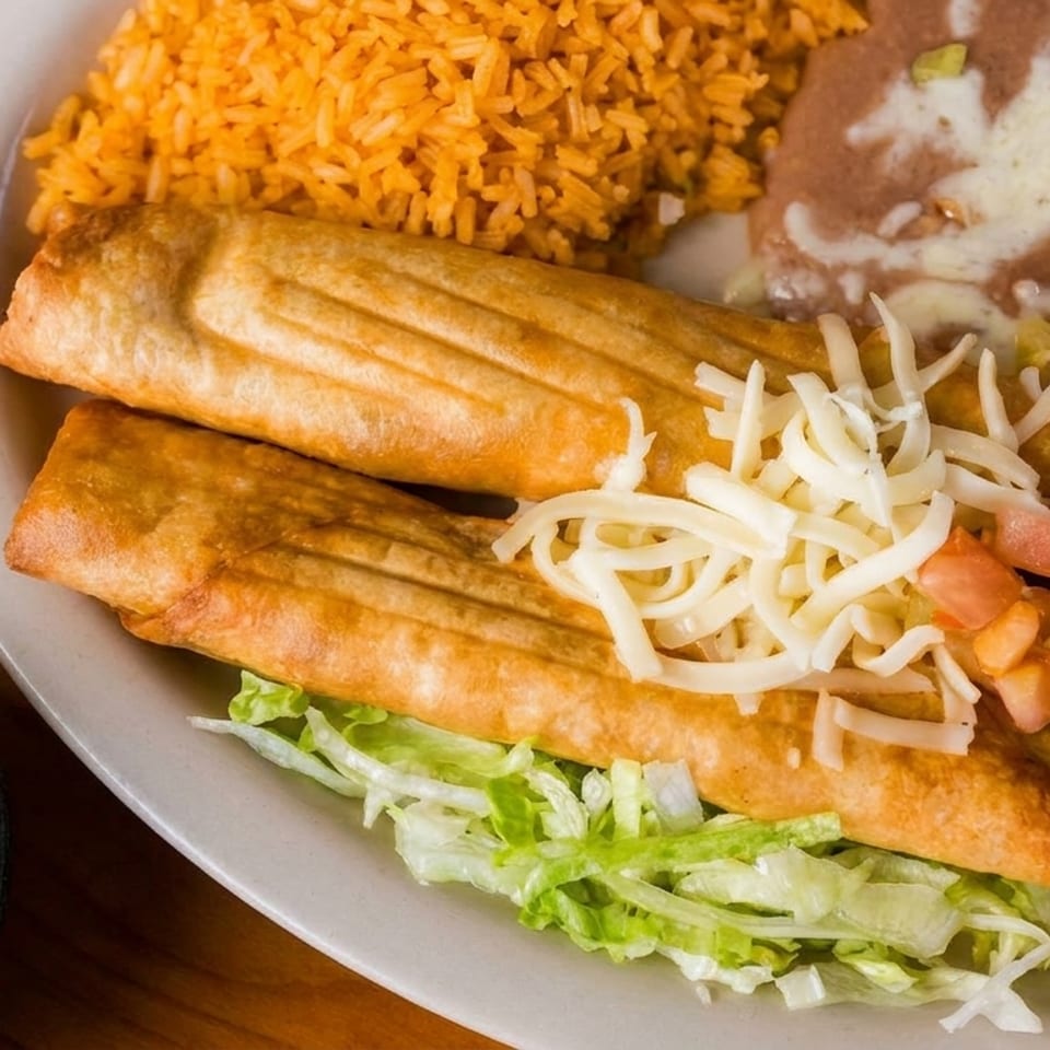 Two golden taquitos on lettuce with rice, refried beans, guacamole, and shredded cheese.