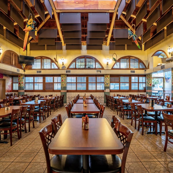 Spacious Mexican restaurant dining room with many wooden tables and chairs, arched windows, and decorative murals.